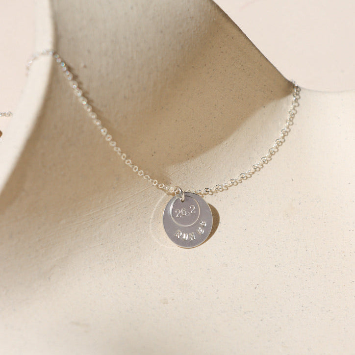 sterling silver hand stamped round disc charms on a delicate chain necklace on a light surface