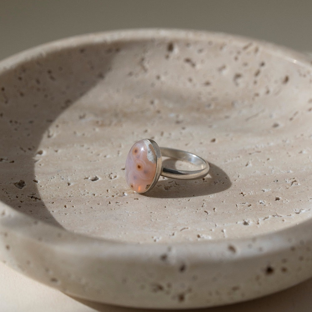 a sterling silver hand-set ocean jasper ring laid out on a cream colored backdrop in the sun