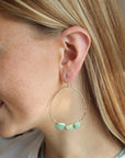 A model wearing a 1.75 wide 14k gold fill wire hoop with three amazonite gemstones wire wrapped at the bottom of each earring. 