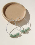 A 1.75 wide sterling silver wire hoop with three amazonite gemstones wire wrapped at the bottom of each earring. Earrings are displayed on a cream back drop. 