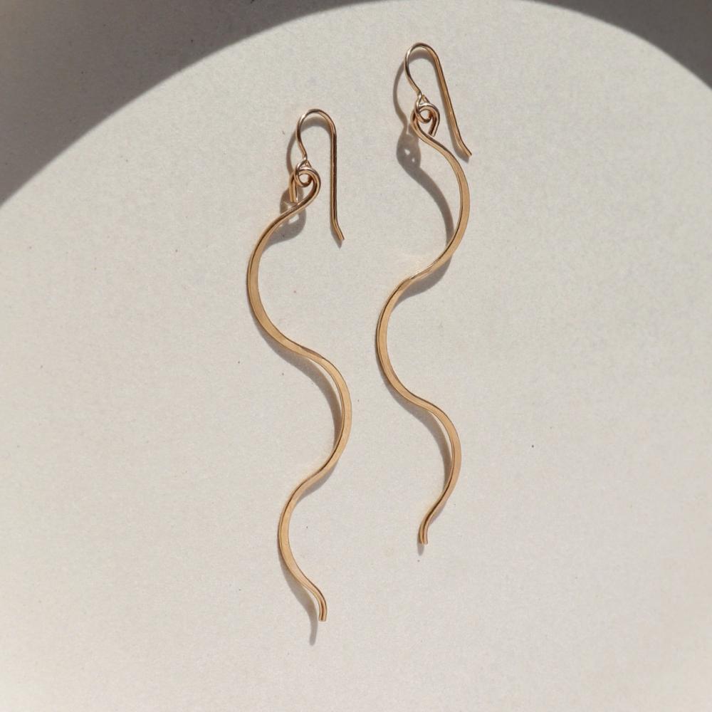 14k gold filled sidewinder earrings laying on a sunlit white dish.