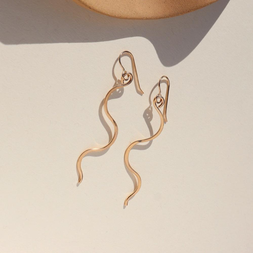 14k gold filled sidewinder earrings laying on a sunlit white dish.