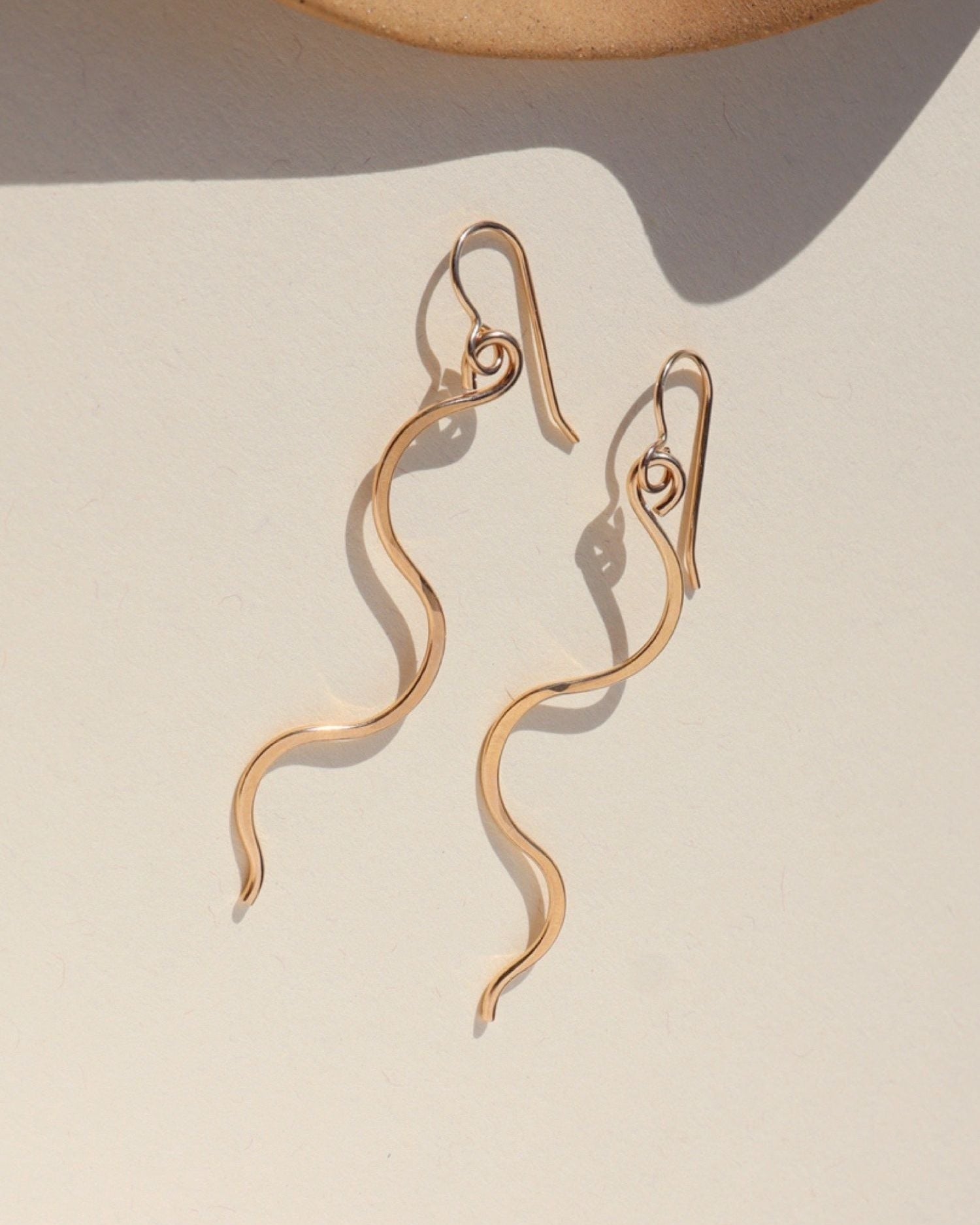 Gold snake-shaped earrings on a textured beige surface