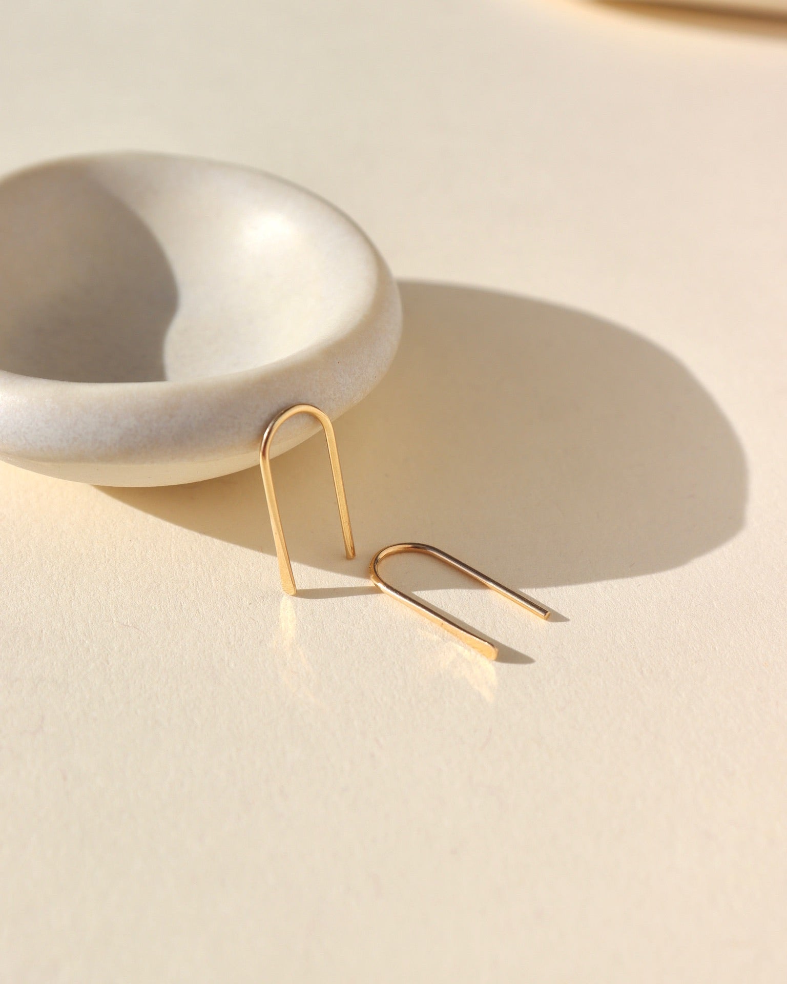 arch shaped 14k solid gold earrings near a small dish in the sunlight