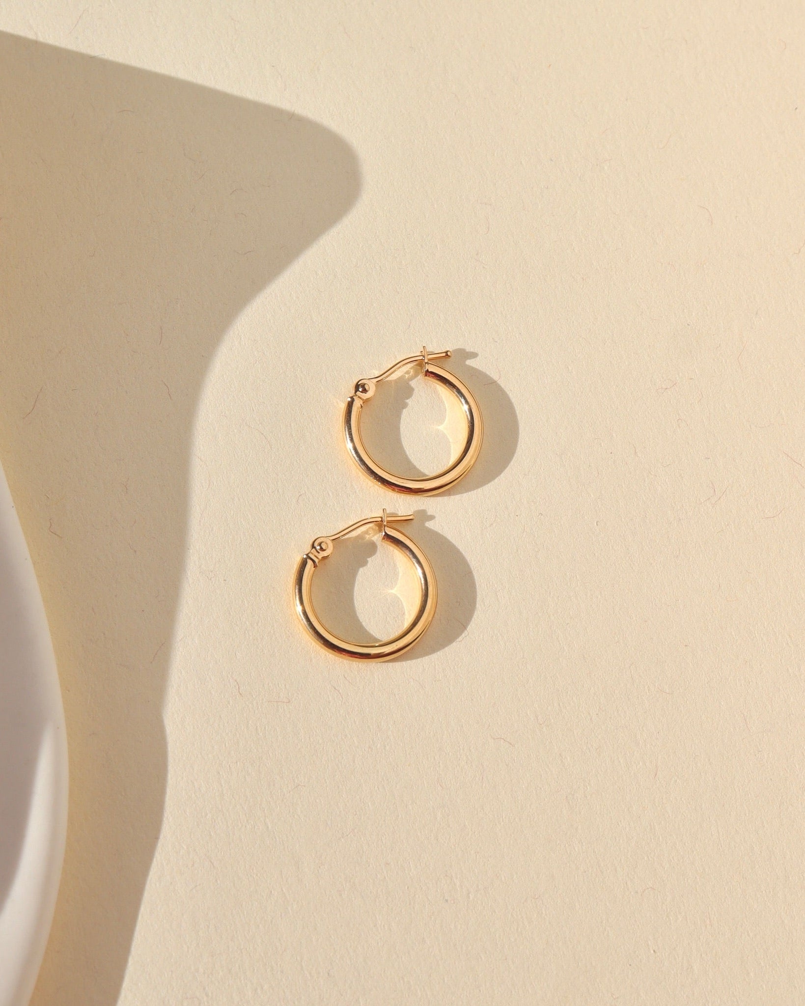 smooth 14k solid gold hoop earrings laid in the sunlight