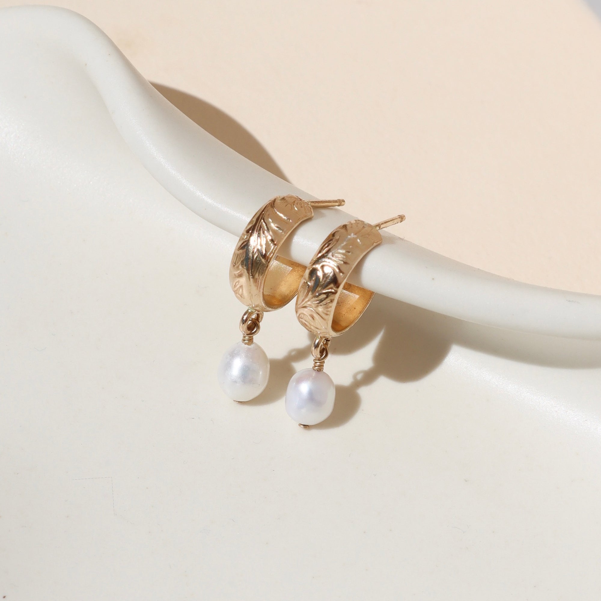 14k gold fill textured hoop earrings with pearl drops on a light dish