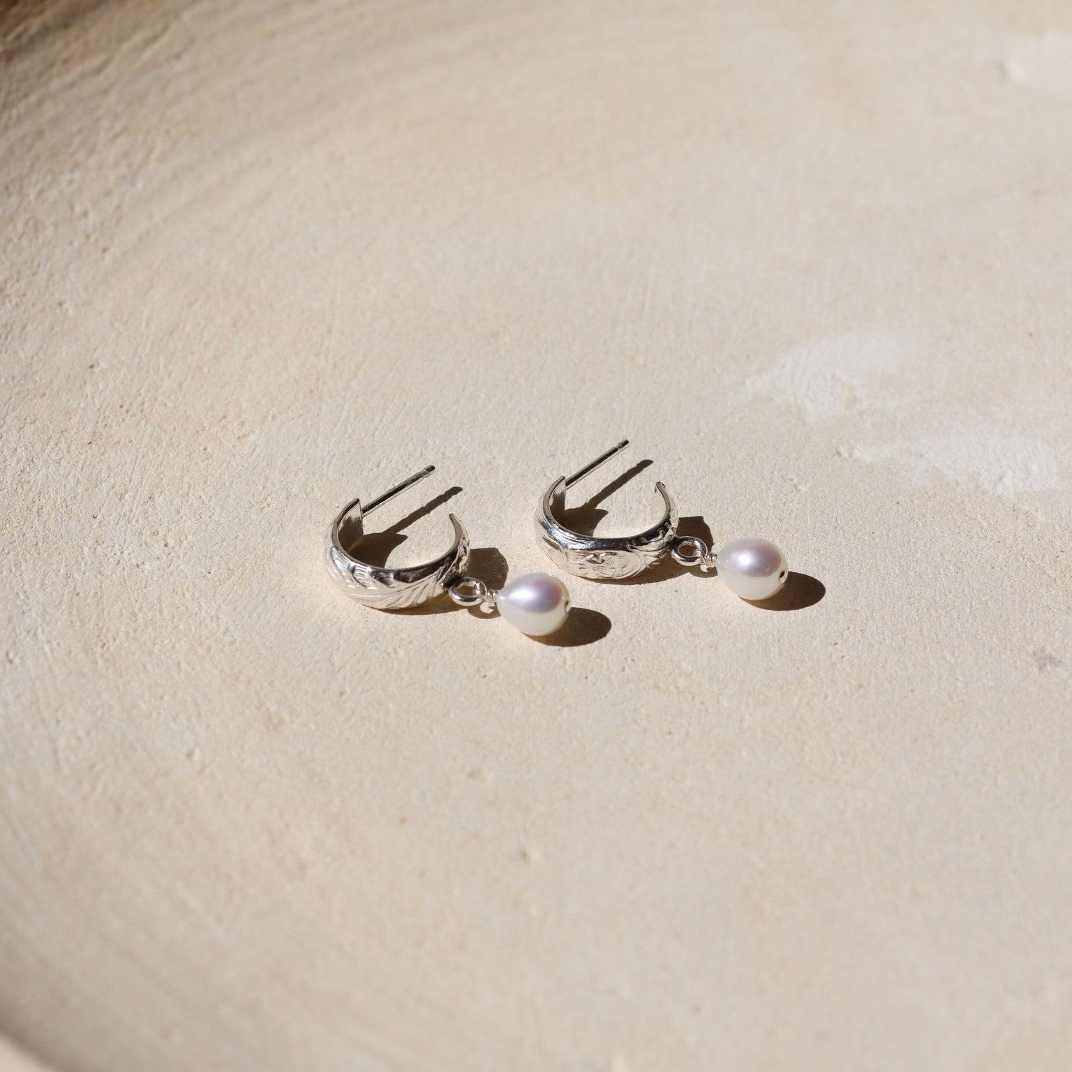 Pair of silver earrings with pearls on a textured beige surface