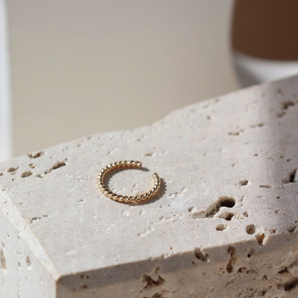 14k gold fill Spiral Ear Cuff laid on a stone plate in the sunlight. This ear cuff features the spiral allusion of a twist of two metals. This ear cuff is easy to wear on your ear.