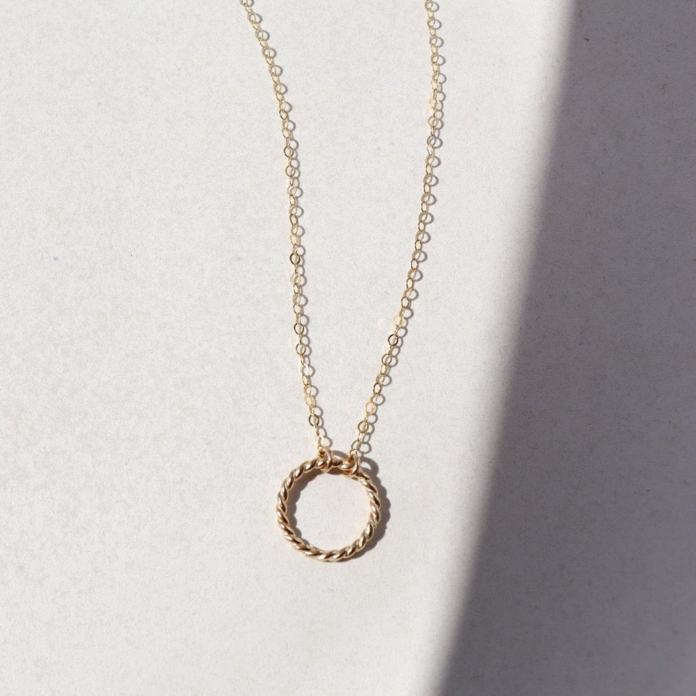 14k gold fill spiral necklace laid on a white plate in the sunlight. This necklace features the simple chain with the spiral eternity disc.