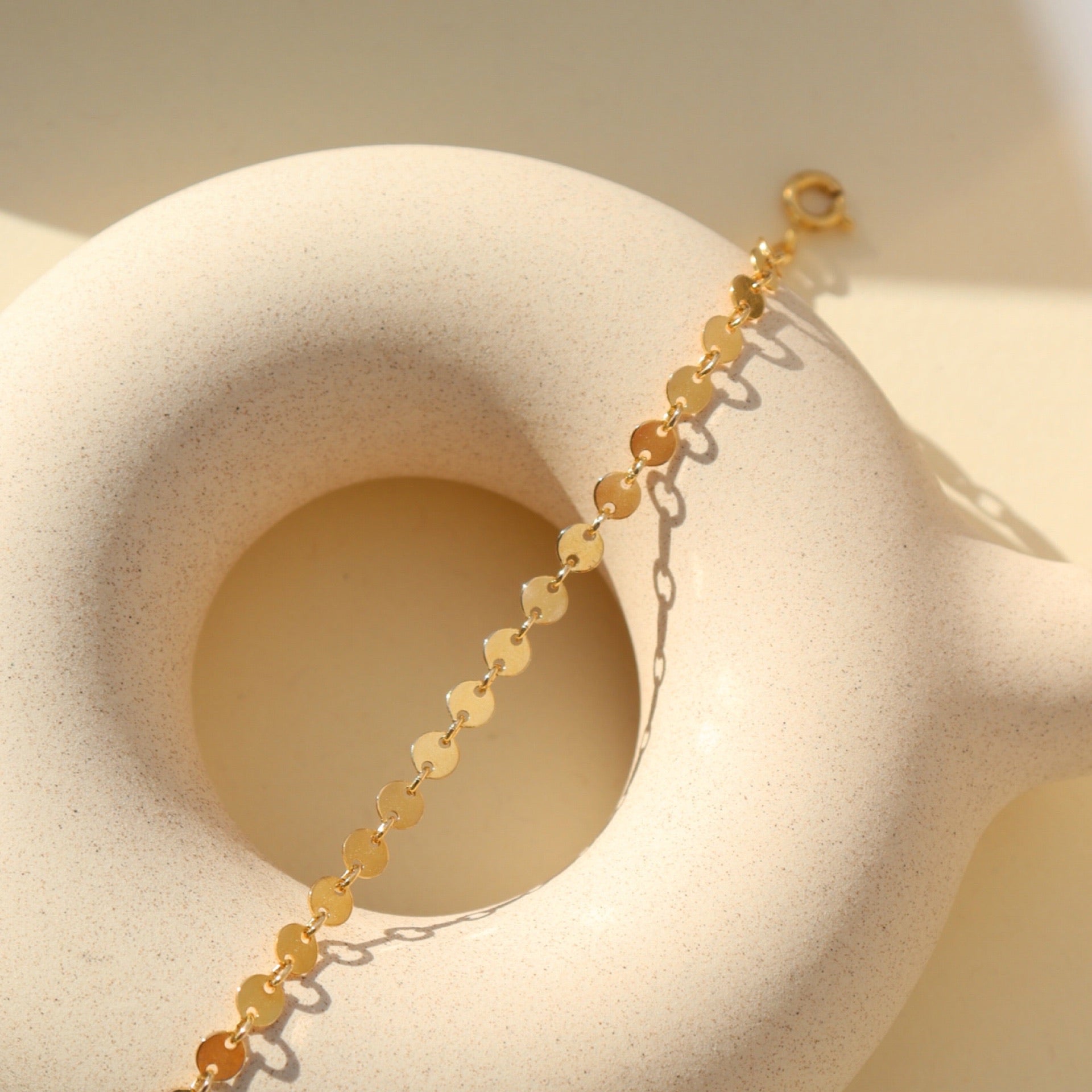 Starlight Bracelet featuring polished disc chain links styled on a textured ceramic form in natural light.