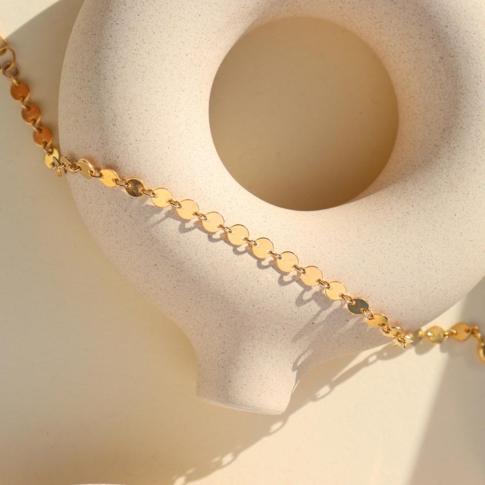 14k gold fill Starlight Choker laid in the sunlight on a gray plate. This choker is perfect for layering. This Necklace features circle disc that are linked together.