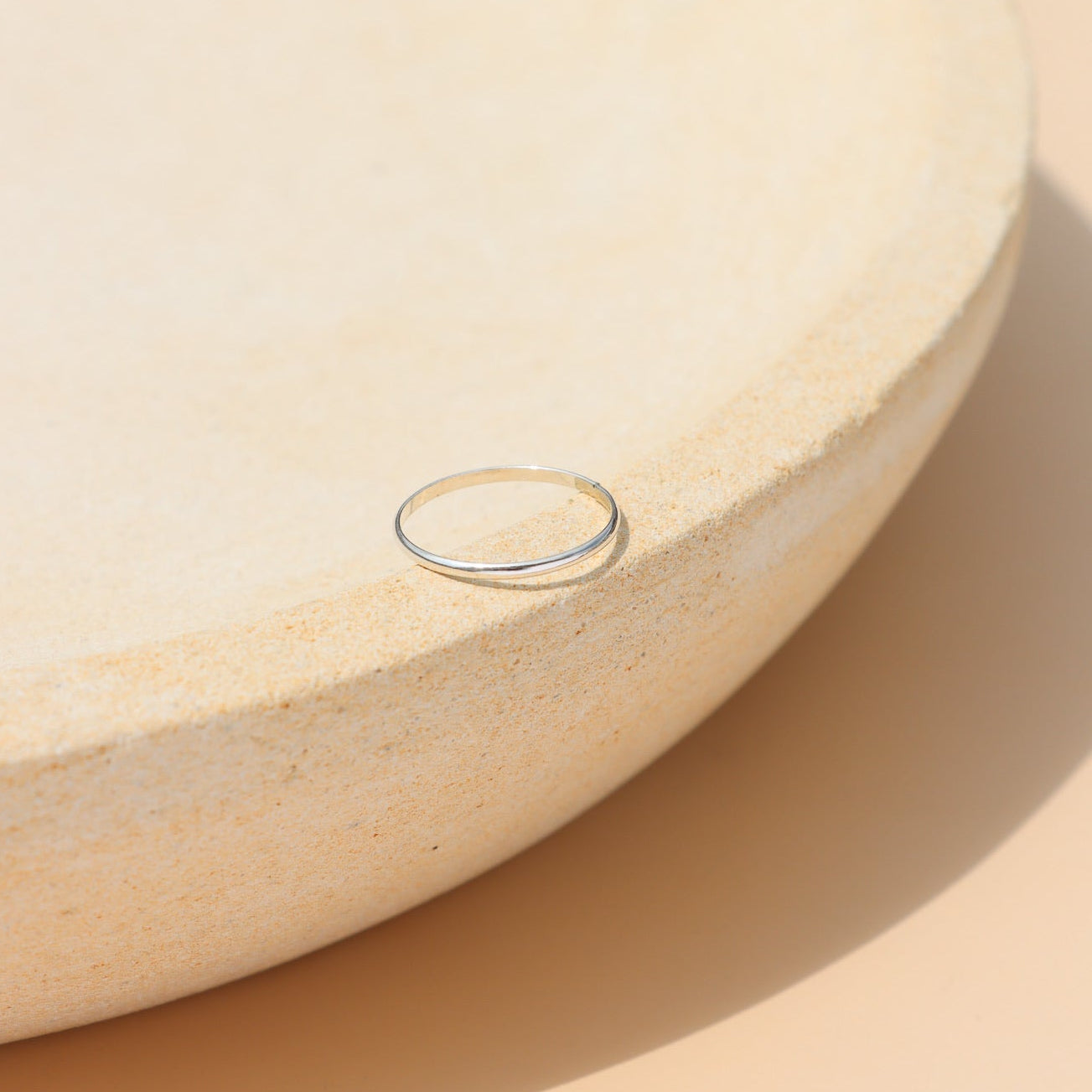Sterling silver minimalist stacking ring with a thin polished band, modern everyday jewelry displayed on a ceramic jewelry tray in natural sunlight.