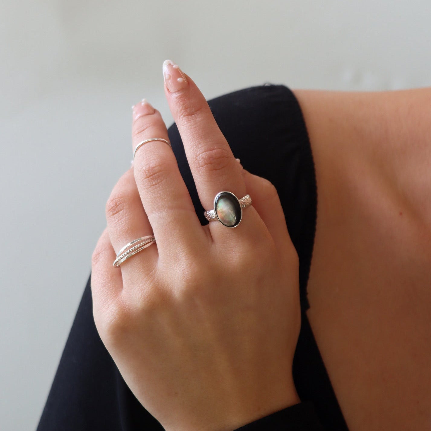 Model wearing a sterling silver oval labradorite statement ring with decorative band details, styled with minimalist sterling silver stacking rings on the hand.