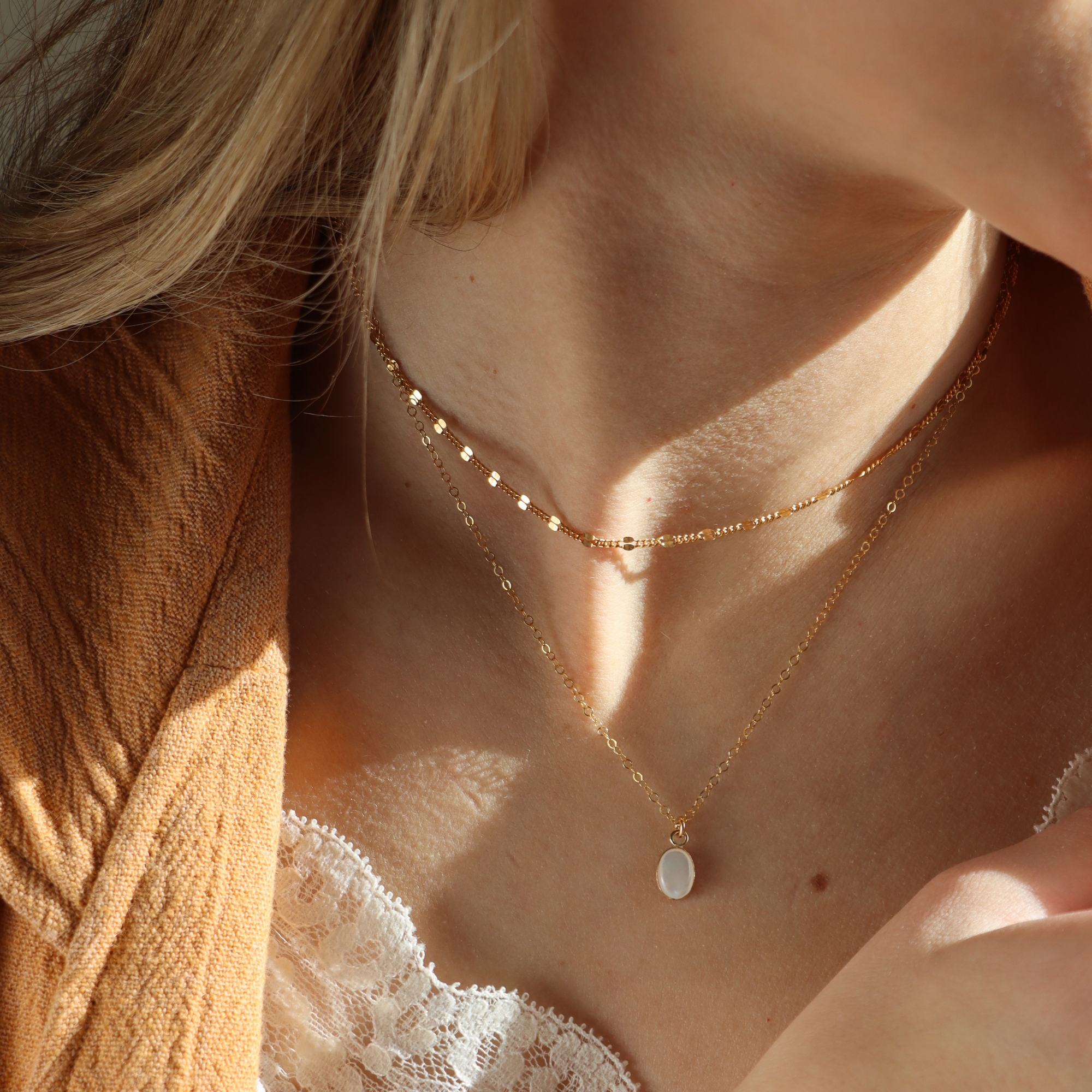 Model wearing a 14k Gold Filled necklace stack with a shiny necklace and a pearl pendant necklace on a simple chain. 