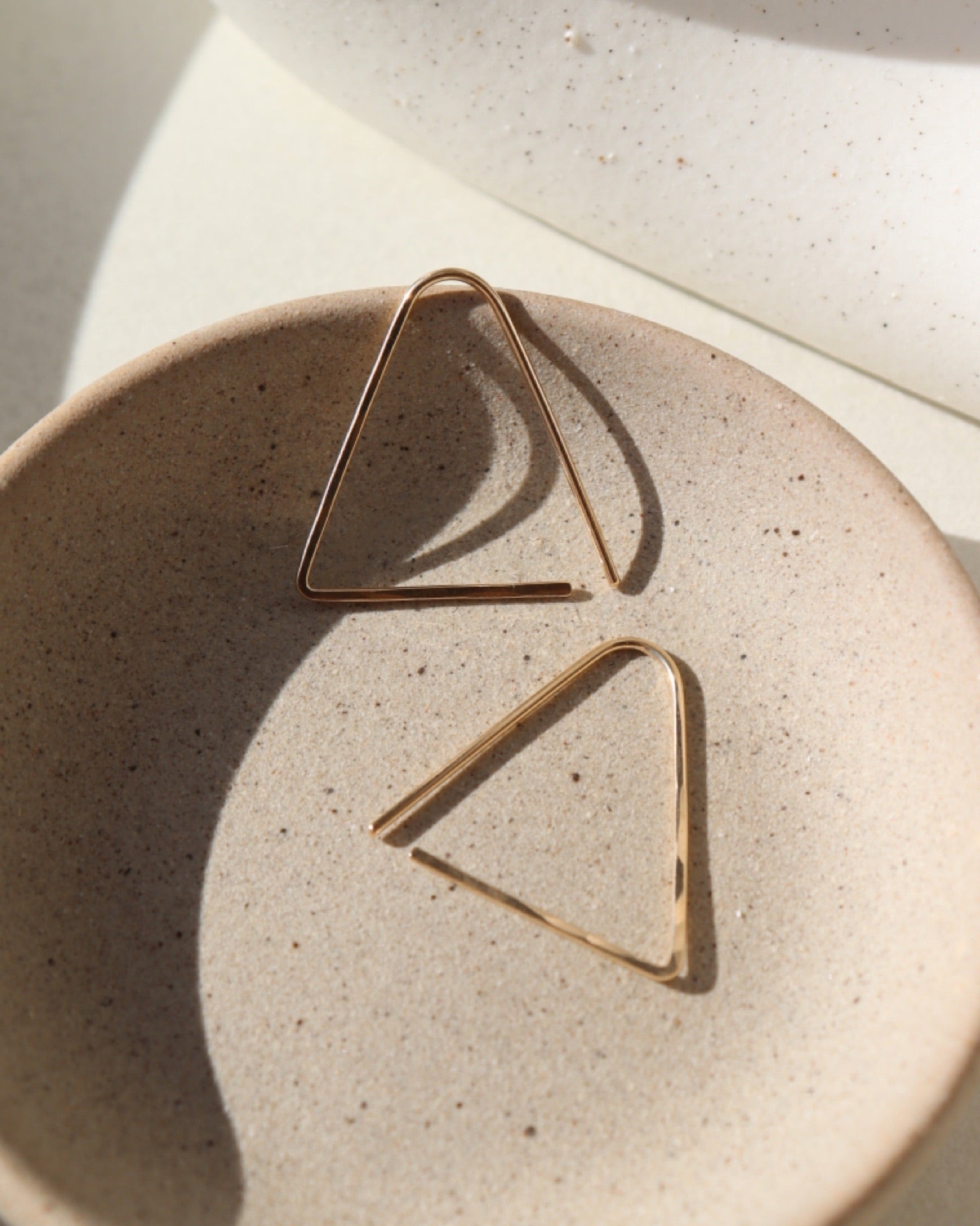 14k gold fill hammered triangle earrings on a light dish