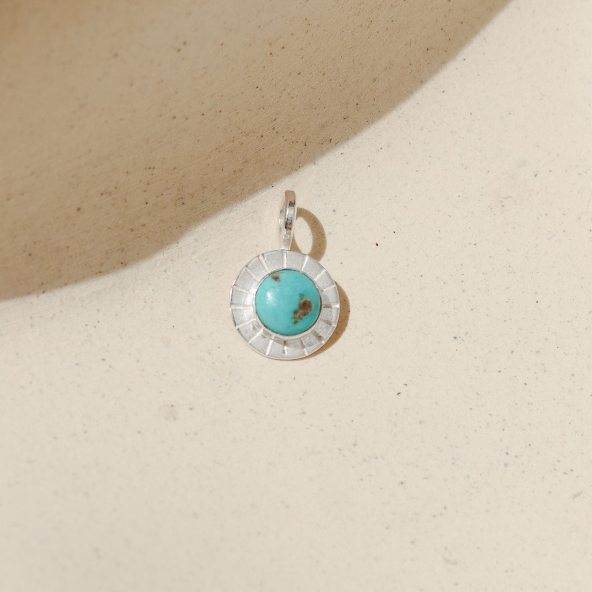 sterling silver round charm with turquoise gemstone on a light dish