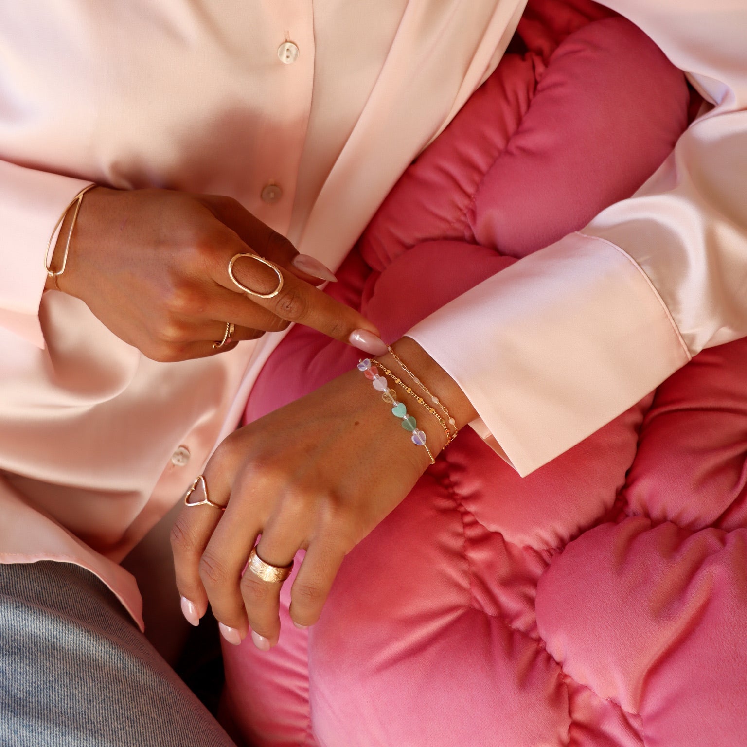 model wearing multiple 14k gold fill rings paired with multicolored heart bead bracelet and 14k gold fill chain bracelets