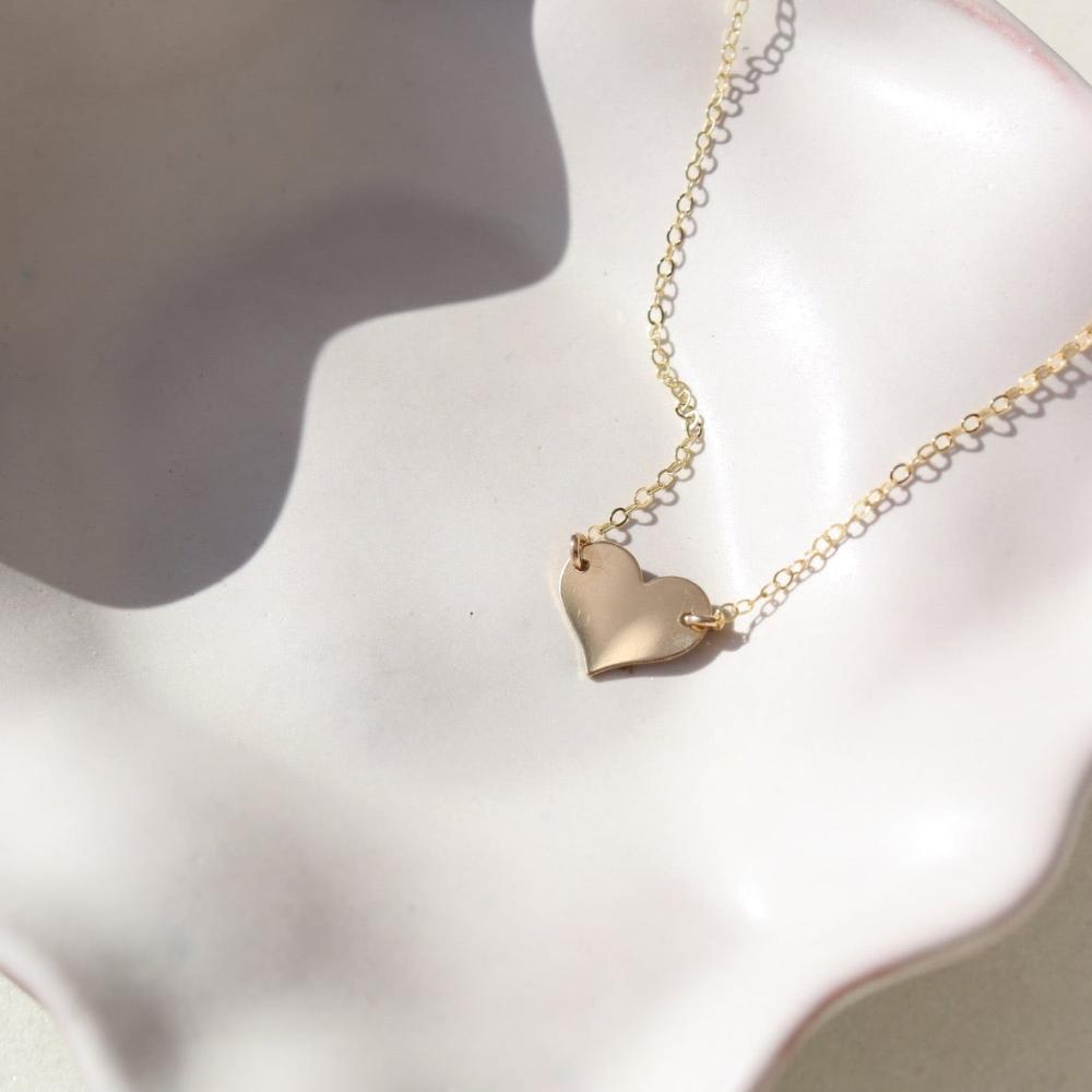 14k gold heart necklace on a 14k gold fill chain, photographed on a ceramic dish