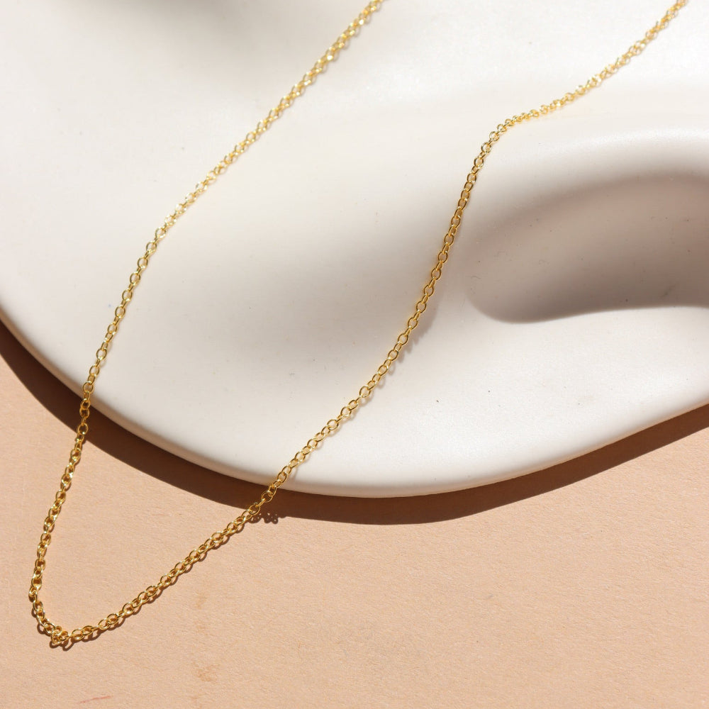A 14k gold fill dainty chain displayed on a cream dish in the sunlight. 