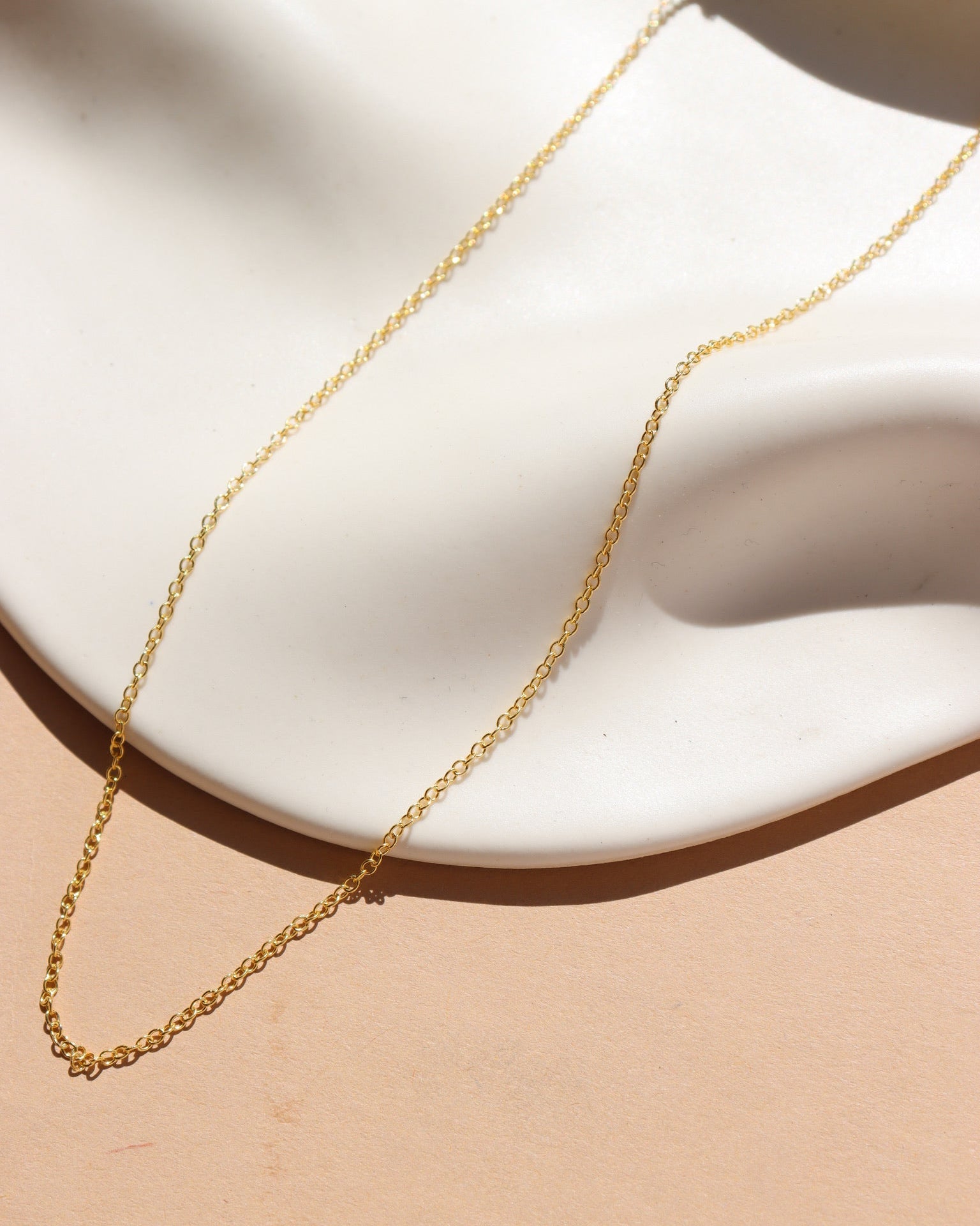 A 14k gold fill dainty chain displayed on a cream dish in the sunlight. 