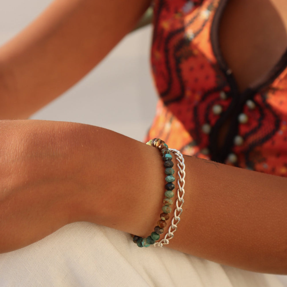 Model wearing Taos Bracelet featuring multicolored turquoise beads in soft blues, greens, and browns with a gold filled spring clasp.