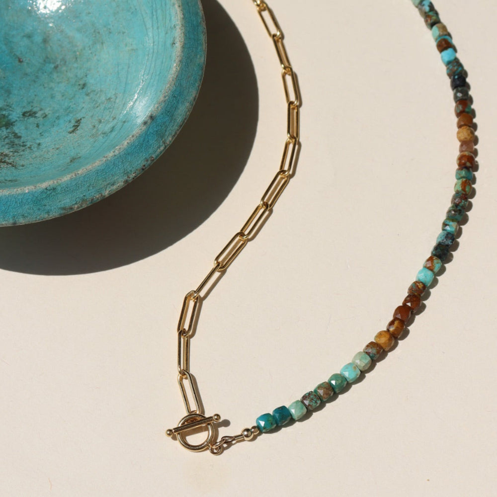 Taos Toggle Necklace featuring half turquoise beads and half gold paperclip chain with a front toggle clasp displayed against a cream back drop 