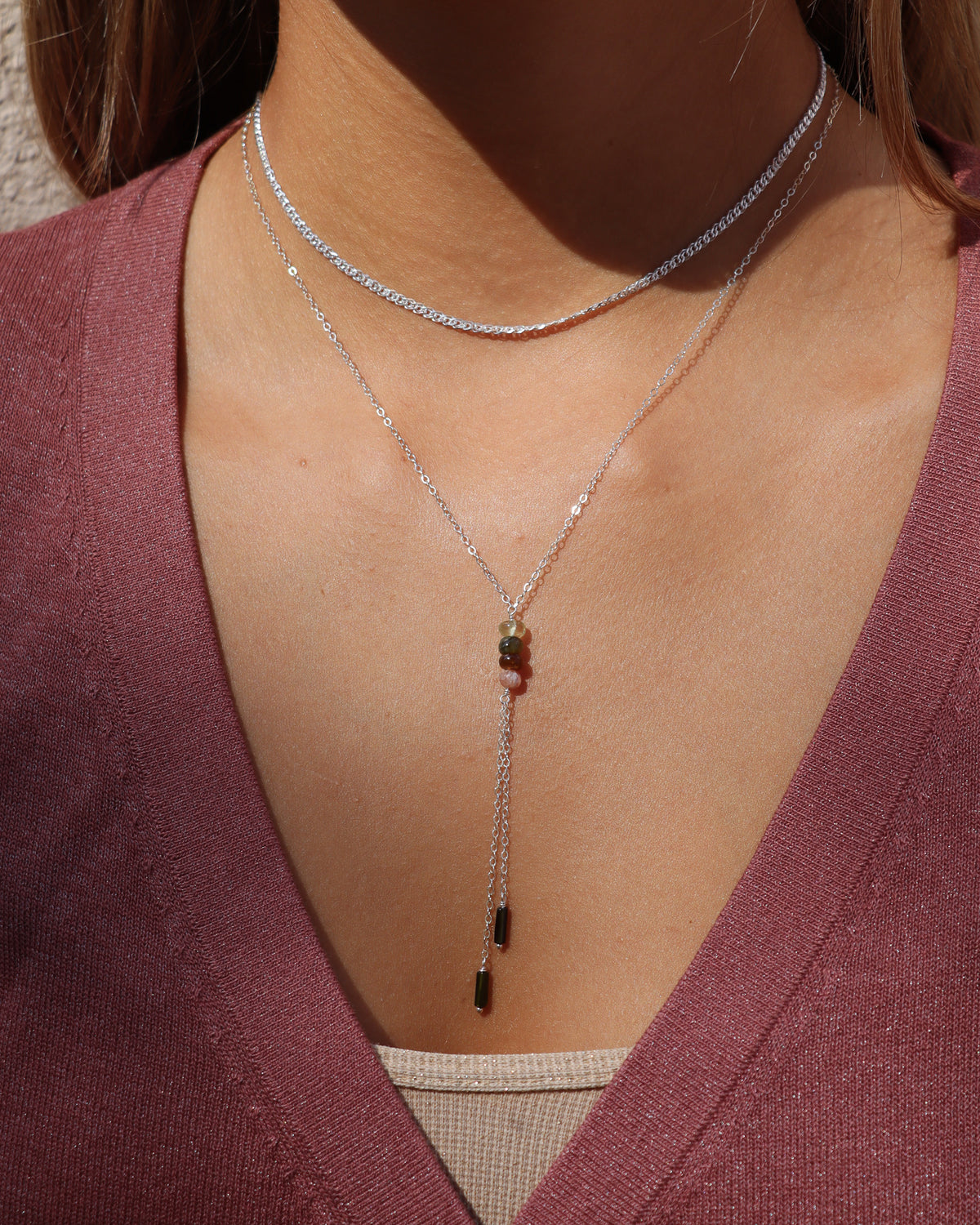 Silver gemstone lariat necklace layered with a silver chain necklace and styled with a mauve top.