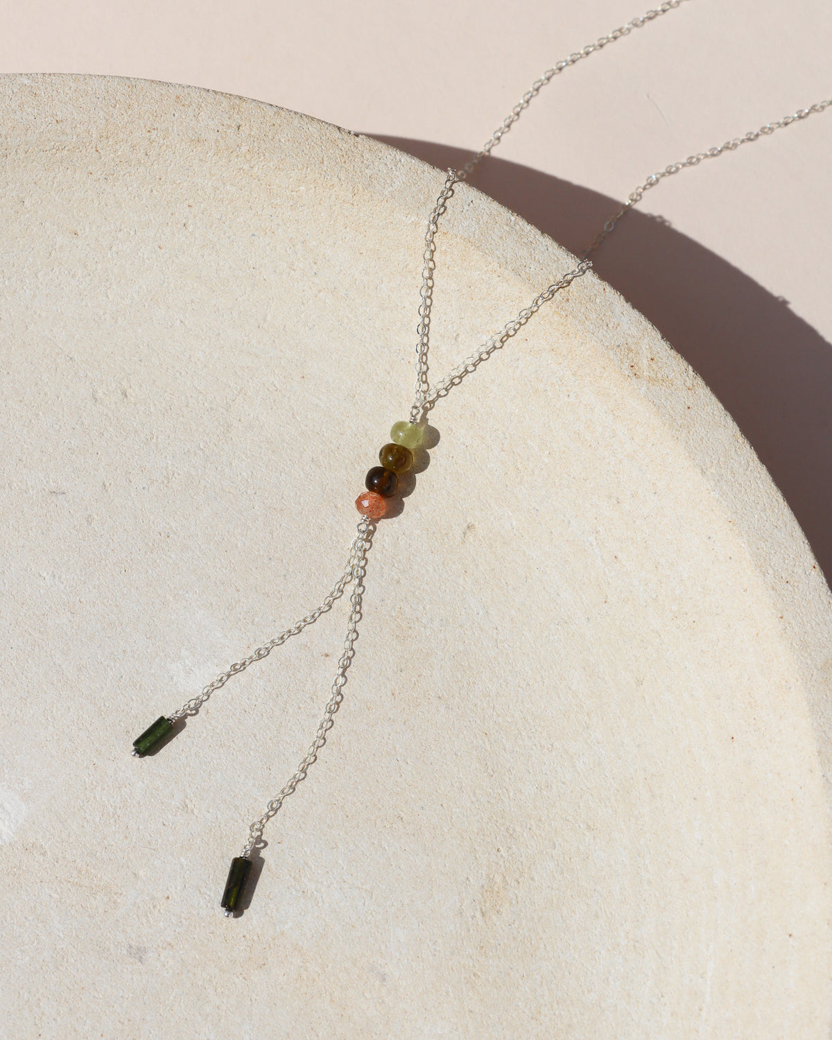 Silver lariat necklace with multicolored gemstone beads and dark green bead accents, displayed in warm sunlight.