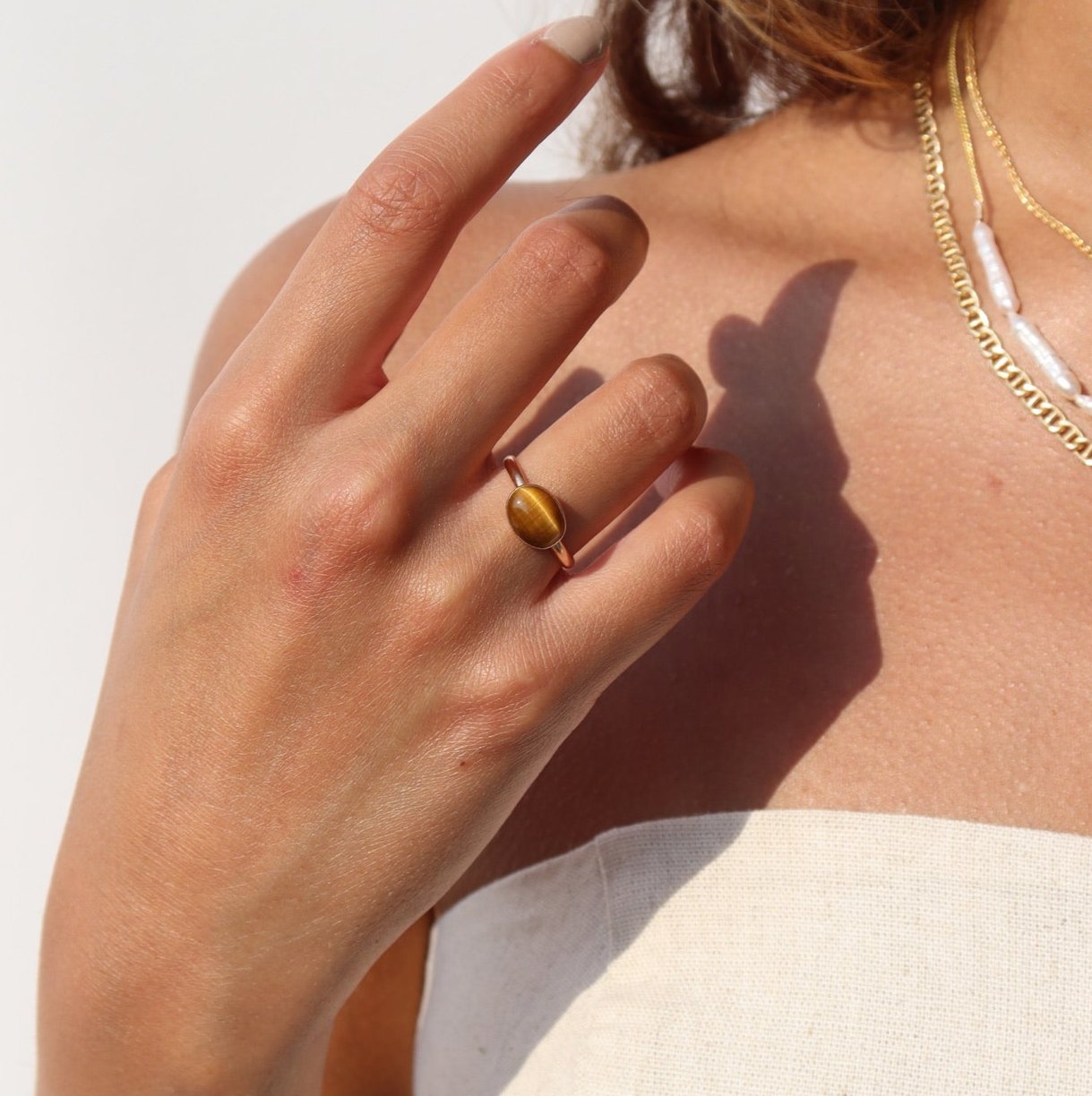 An amber-colored Tiger Eye gemstone on a horizontal bezel on a 14k gold fill band, photographed on a model