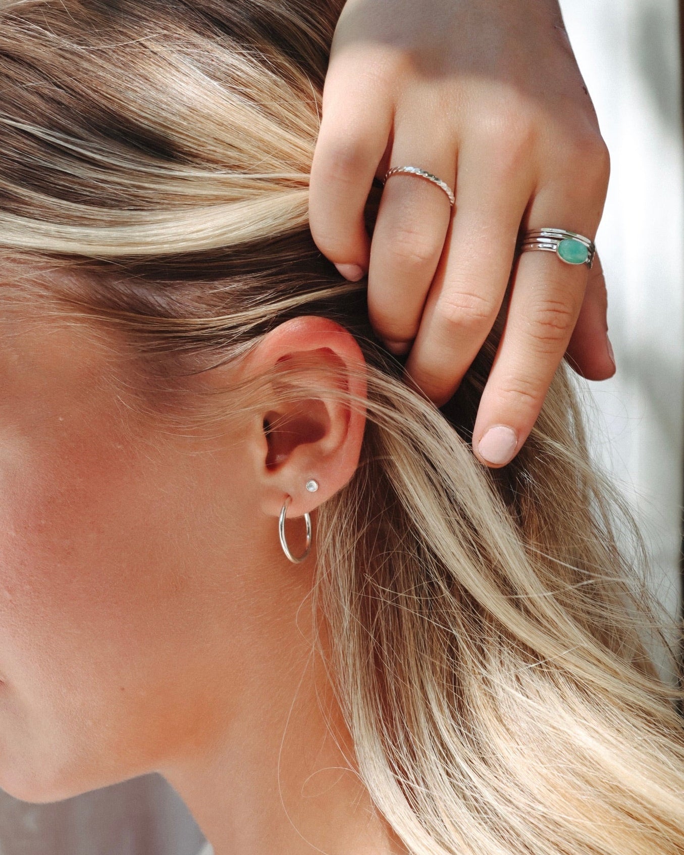 Close-up of a woman wearing silver hoop and stud earrings with stacked silver rings, including a turquoise gemstone ring.