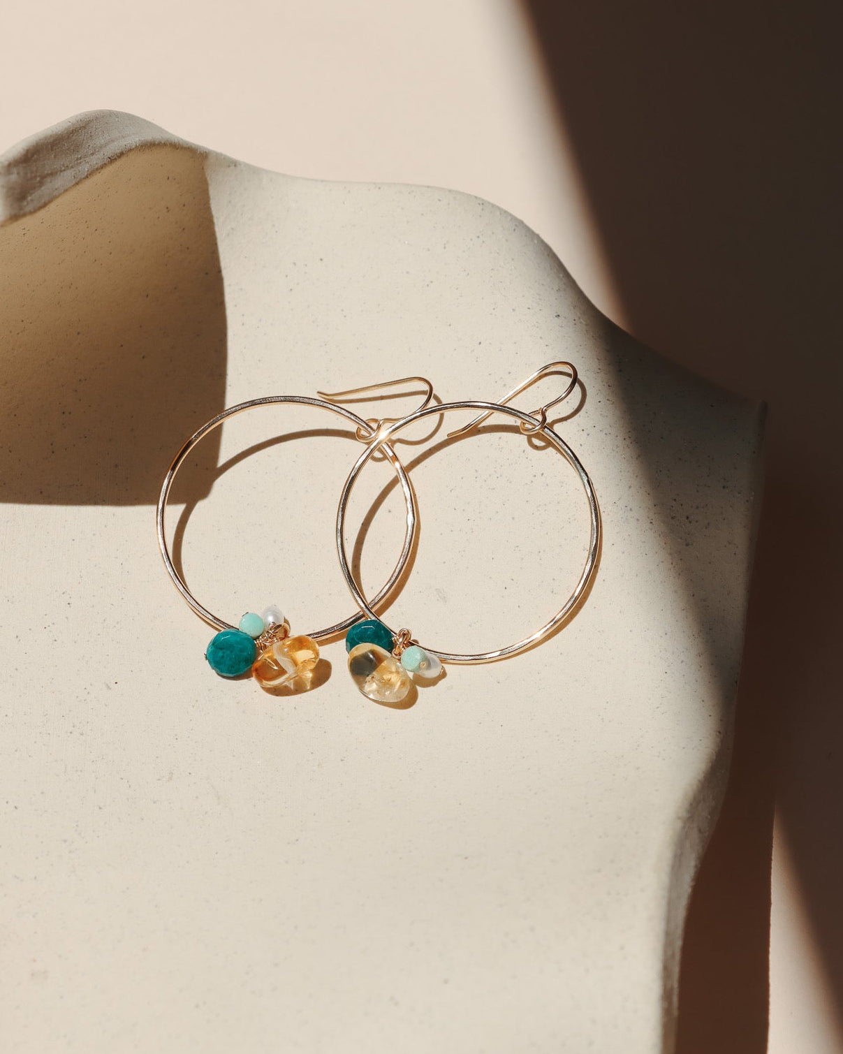 14k gold fill round hoops with gemstone drops on a light dish