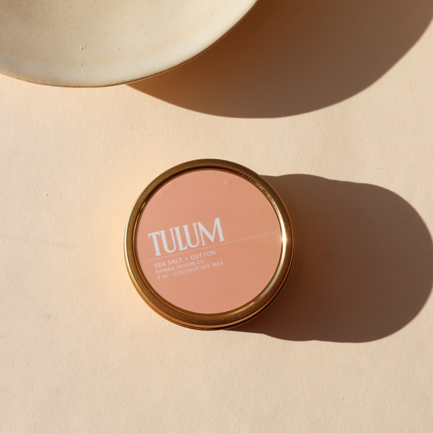 candle in peach colored tin in the sunlight