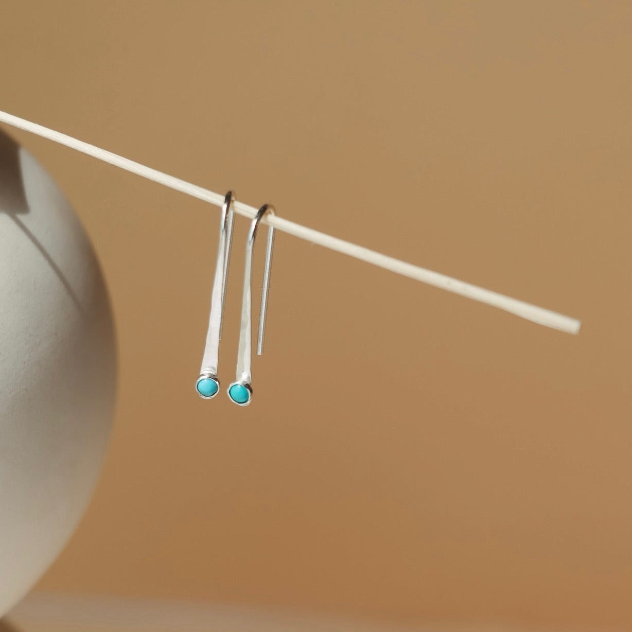 sterling silver arc shaped earrings with a round turquoise stone in the sunlight