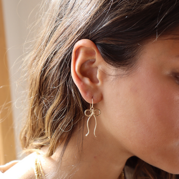 delicate 14k gold fill bow earring on a hook hand made by Token Jewelry, photographed on a model