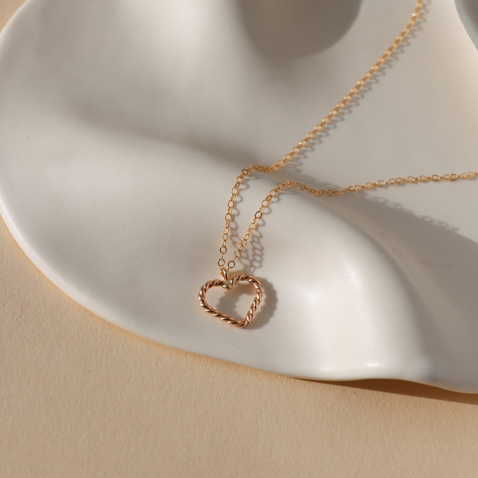 spiral wire heart shaped pendent in 14k gold fill on a simple 14k gold fill chain displayed on a wavy plate