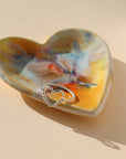 sterling silver spiral heart shaped ring displayed on multicolored heart dish