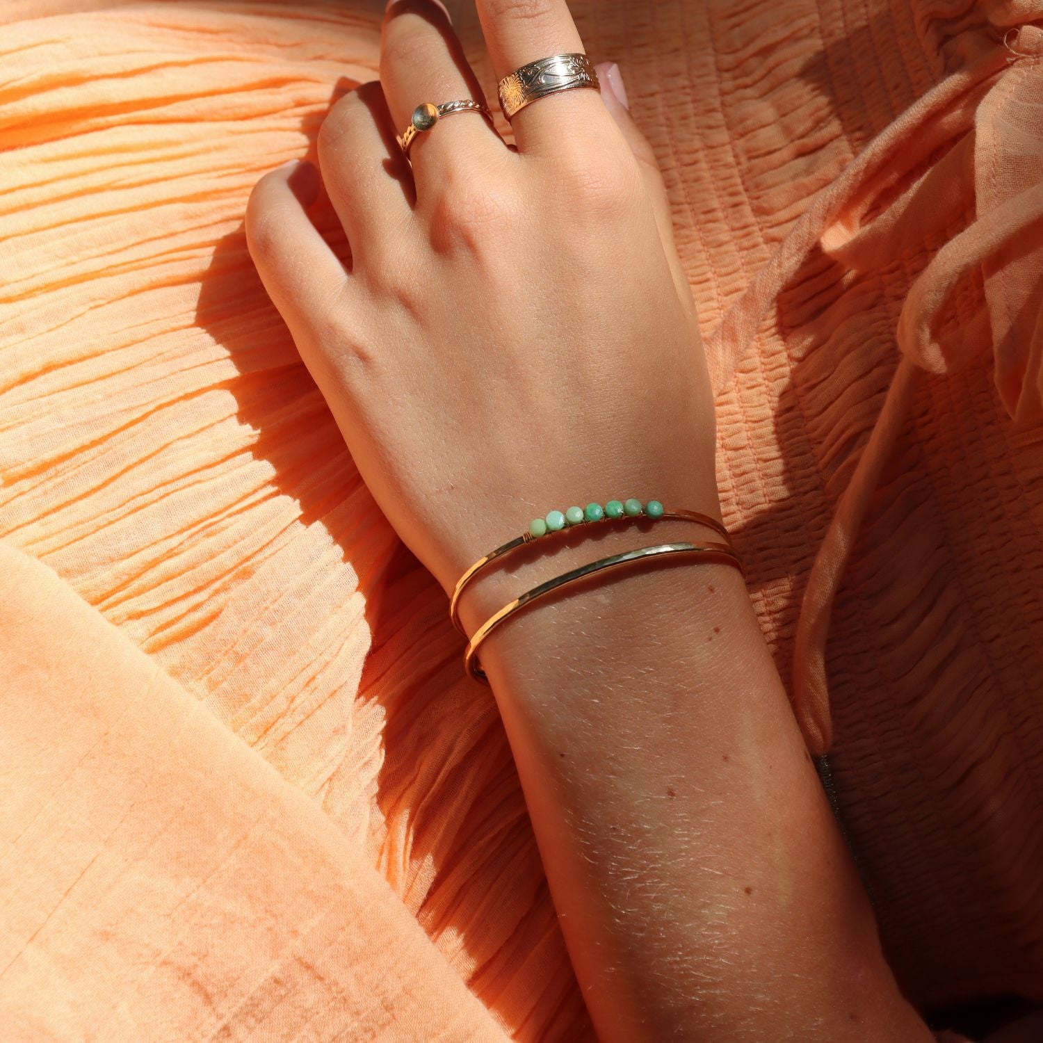 model wearing 14k gold fill jewelry including a cuff with wire wrapped chrysoprase stones in the sunlight
