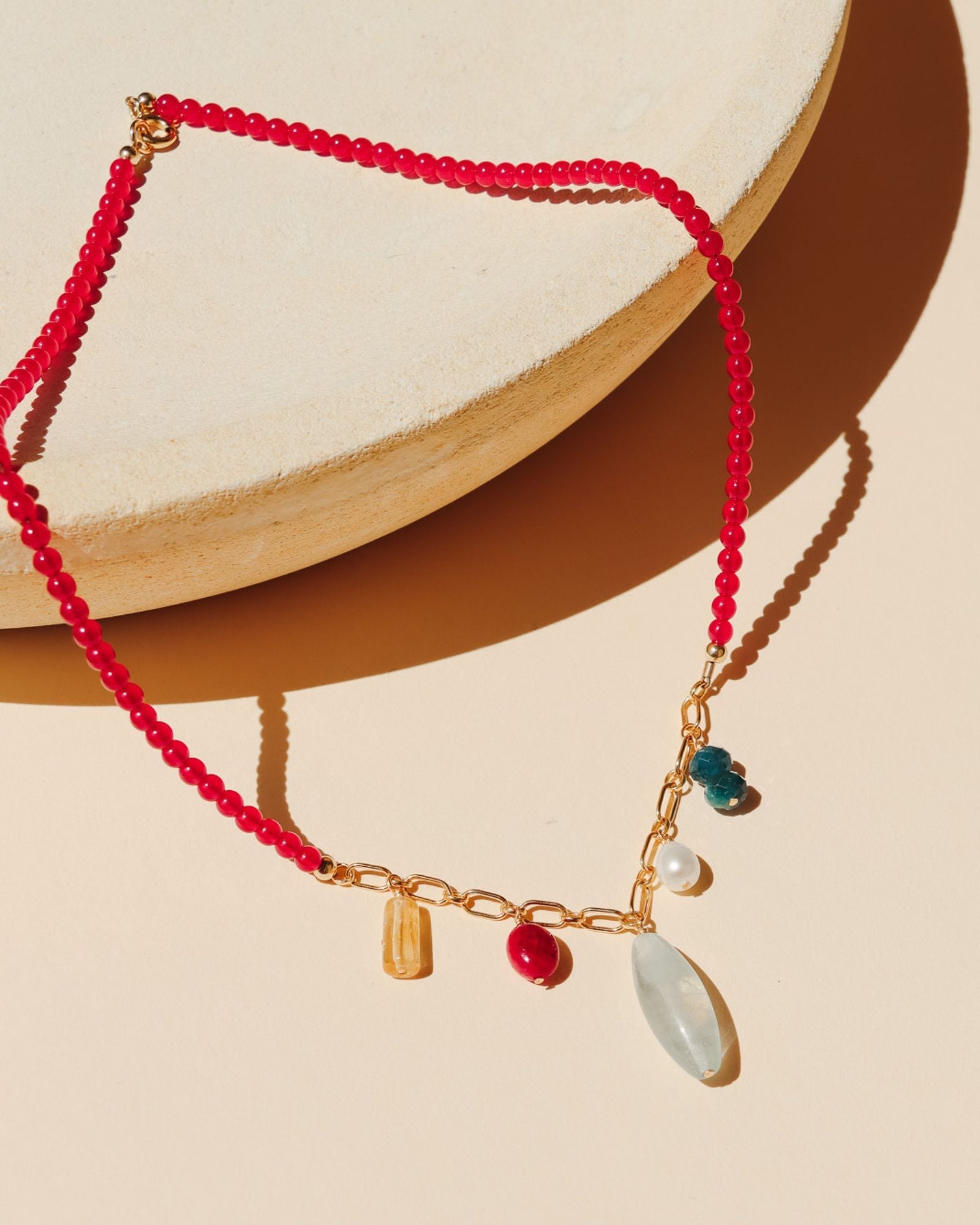 necklace with ruby beads and gold chain with gemstone charms on a light dish