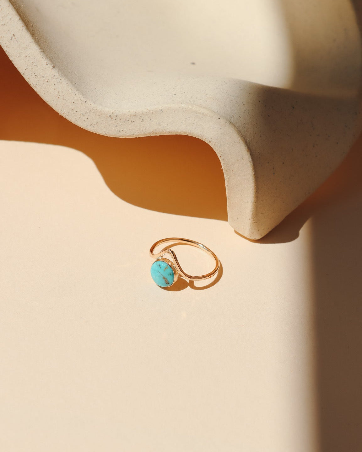 14k gold fill ring with point and round turquoise stone on a light dish