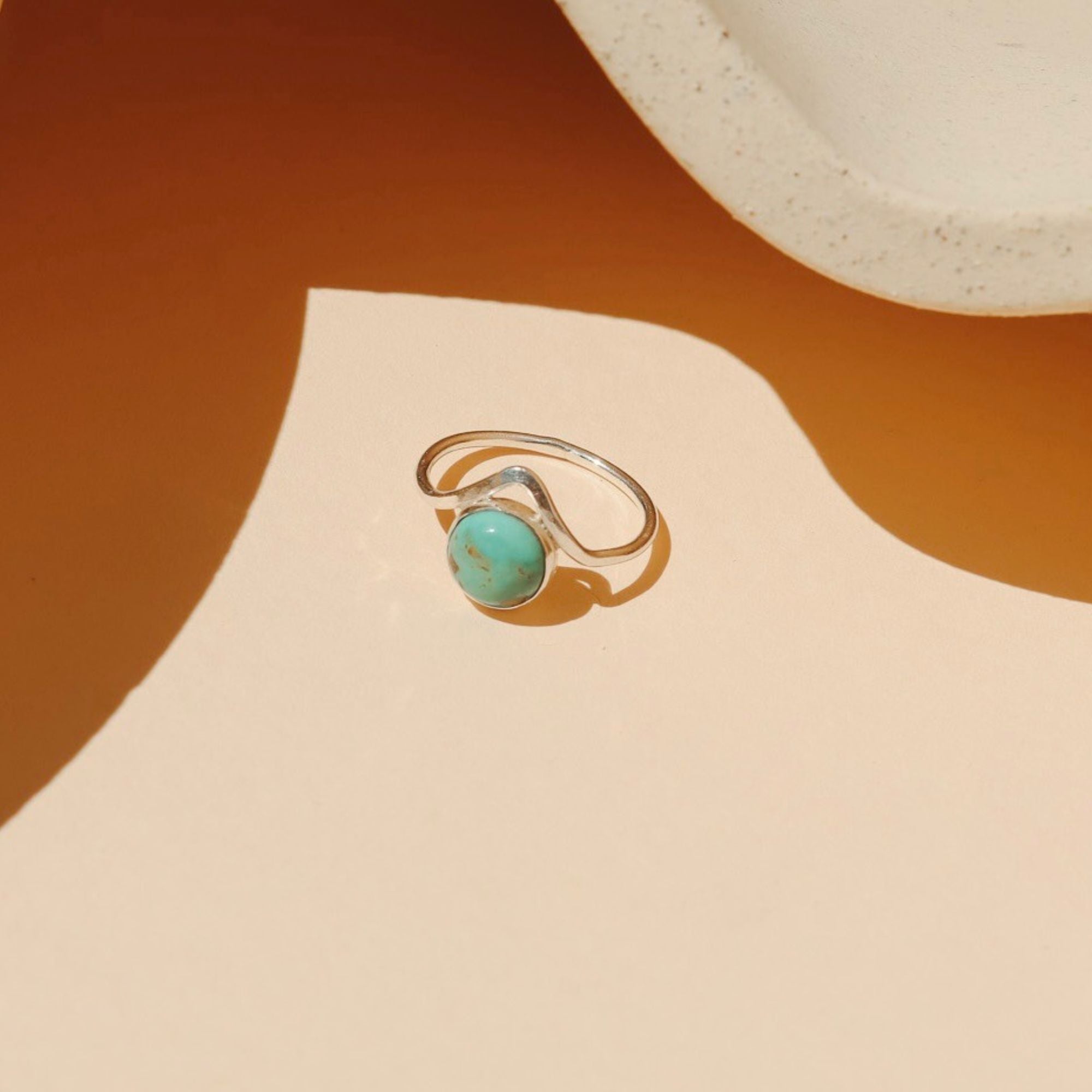 sterling silver ring with point and round turquoise stone on a light dish