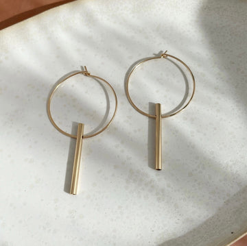 14k gold fill Tunnel Hoops laid on a white plate in the sunlight. These earring feature the the organic hoops with a cilender tube. 