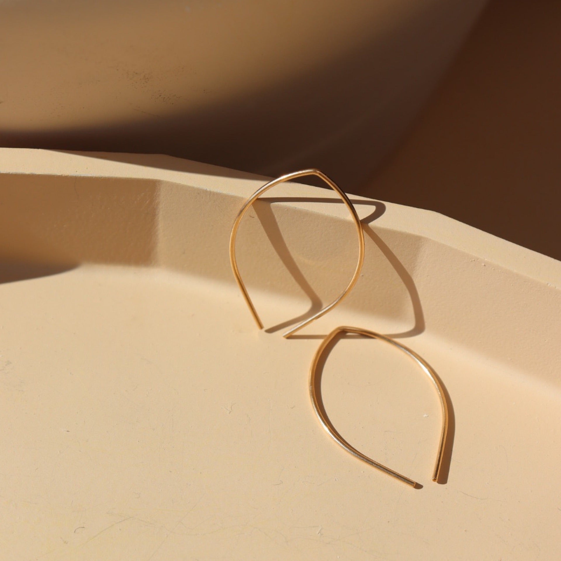 14k gold fill Petal earrings laid on a peach colored plate in the sunlight.