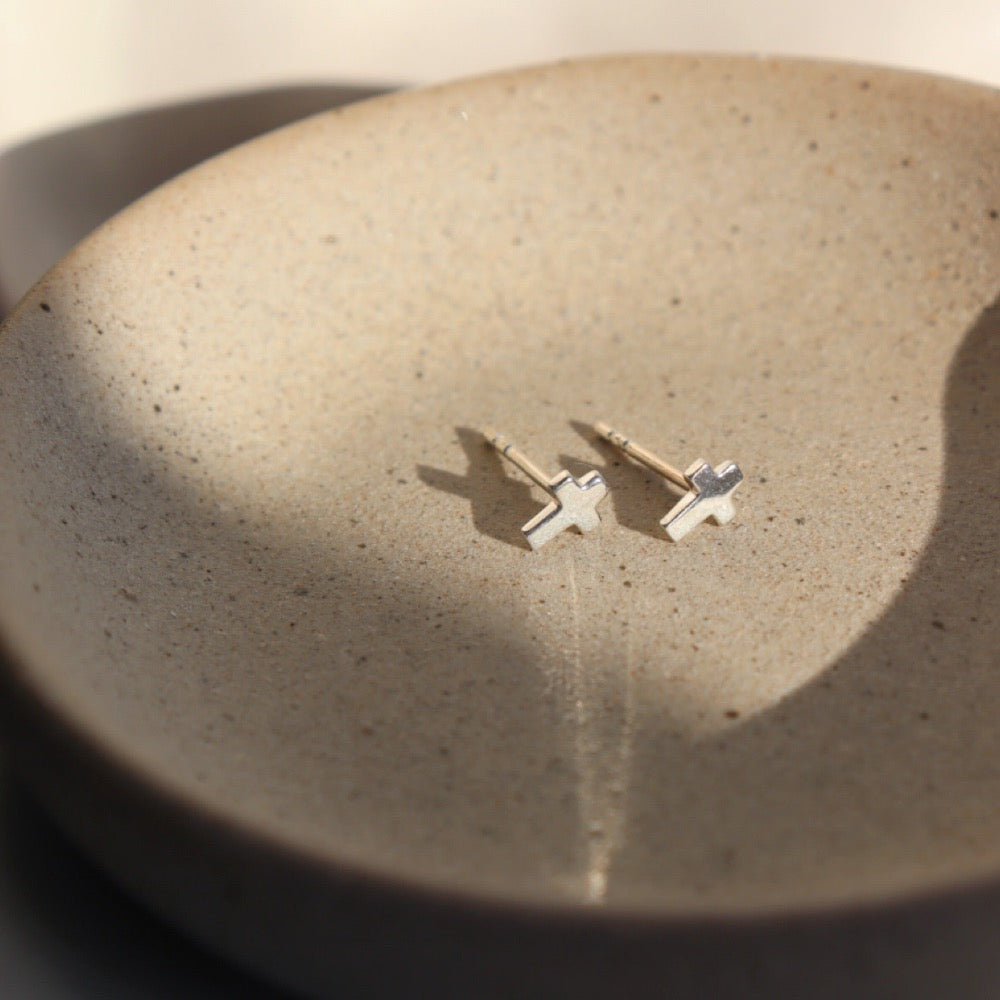 925 Sterling Silver cross stud earrings. Sitting on a gray plate sitting in the sunlight.