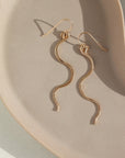14k gold fill Sidewinder earrings placed on a tan plate. These sidewinders feature a snake like look to them with a hook earring. 