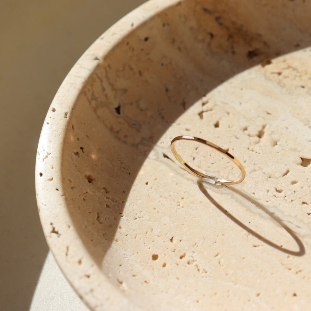 14k gold fill Stacking Ring placed on a tan plate in the sunlight. This ring features a simple band with hammering on the outside.  - Token Jewelry