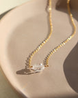 a clear double terminated quartz gemstone, known as a Herkimer Diamond, hangs from a delicate gold filled oval cable chain and is displayed on a ceramic jewelry dish