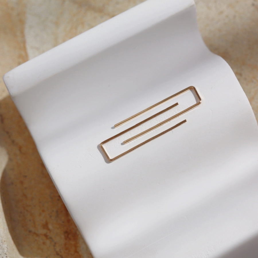 14k gold fill Staple earrings laid on a white plate one the sunlight. A minimal earring that's perfect for everyday. Wear them in your second ear holes or let them be the main adornment for your ear lobes! Either way, these earrings will become one of your daily staples (pun, intended!).