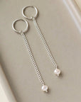 delicate chain hanging from a small hoop earring, with a small pearl at the end