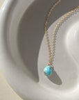 beautiful turquoise stone on a gold chain, lying on a sunlit ceramic dish