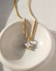 square cut cubic zirconia pendant set in a gold filled bezel and hanging from a delicate box chain sitting on a white jewelry dish.